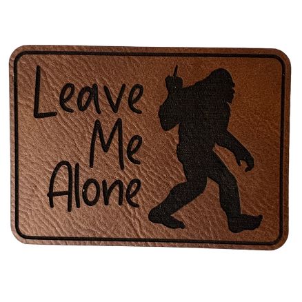  Image of the "Bigfoot - Leave Me Alone" Dark Brown Faux Leather Patch, featuring a humorous Bigfoot silhouette design, perfect for adding a touch of whimsy to any garment or accessory.