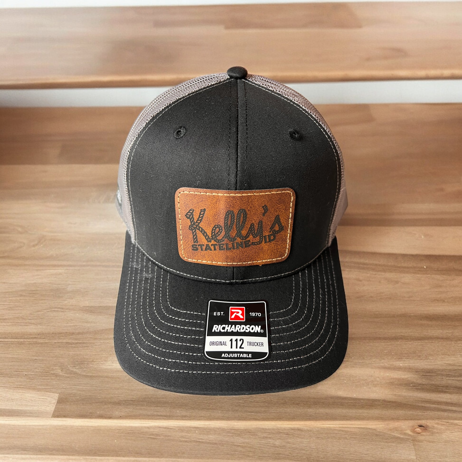 Image of the Kelly Hughes Stateline Richardson Cap in Black/Charcoal, featuring a dark brown patch and integrated ID slot, perfect for showcasing style and convenience at events with durable construction and a comfortable fit.