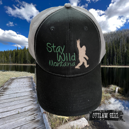 Image of the "Bigfoot Stay Wild Montana" Sandwich Trucker Cap in Black/Gray, showcasing the bold "Stay Wild" message alongside the iconic Bigfoot silhouette, perfect for adventurers and nature enthusiasts.